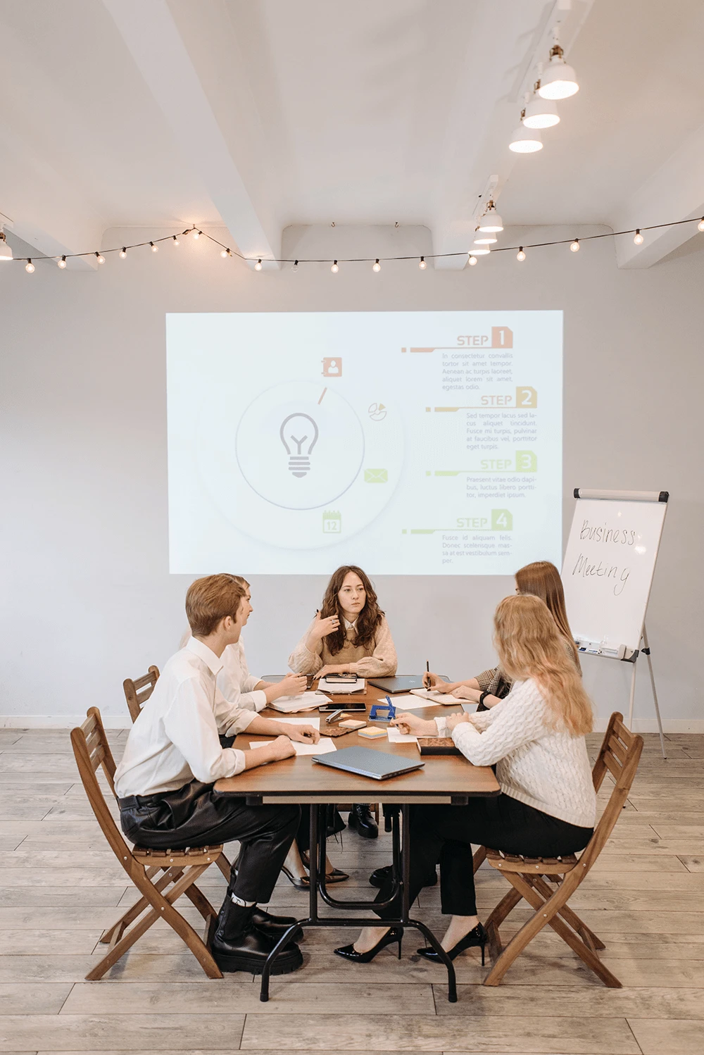 Five people sitting around a table and looking at a presentation on the wall