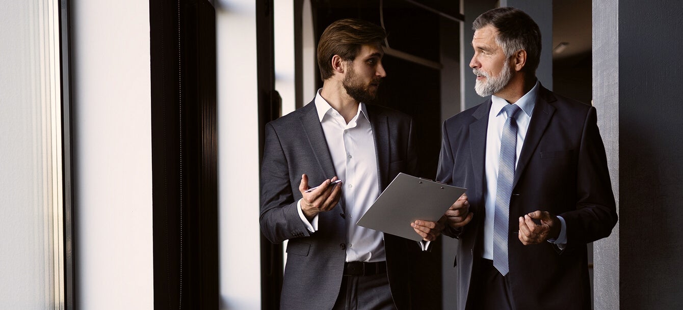 A man in suit holding a clipboard and talking to another man