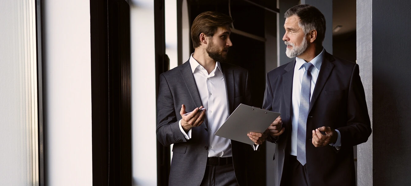 A man in suit holding a clipboard and talking to another man