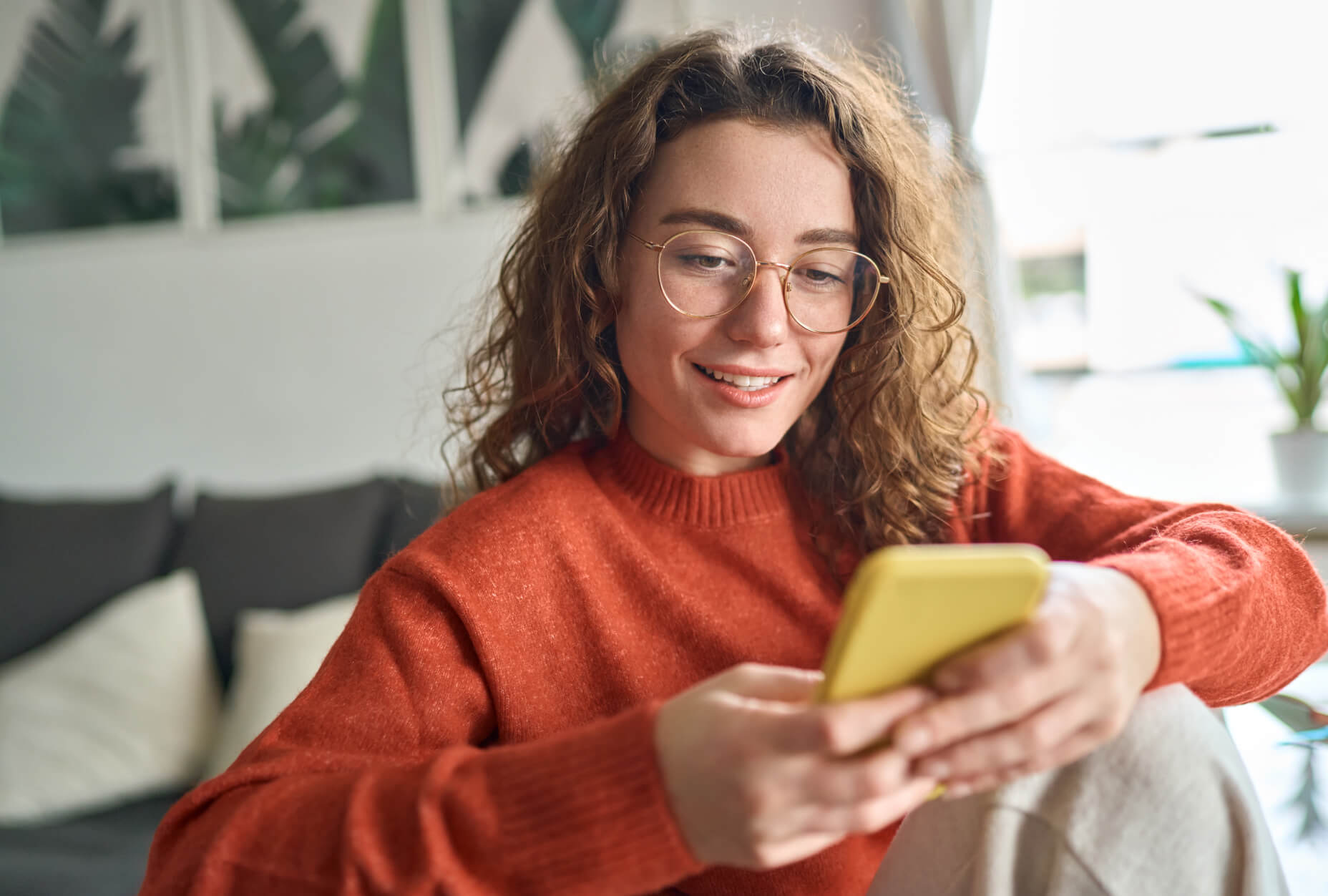 A woman wearing glasses and a red sweater looking at a phone