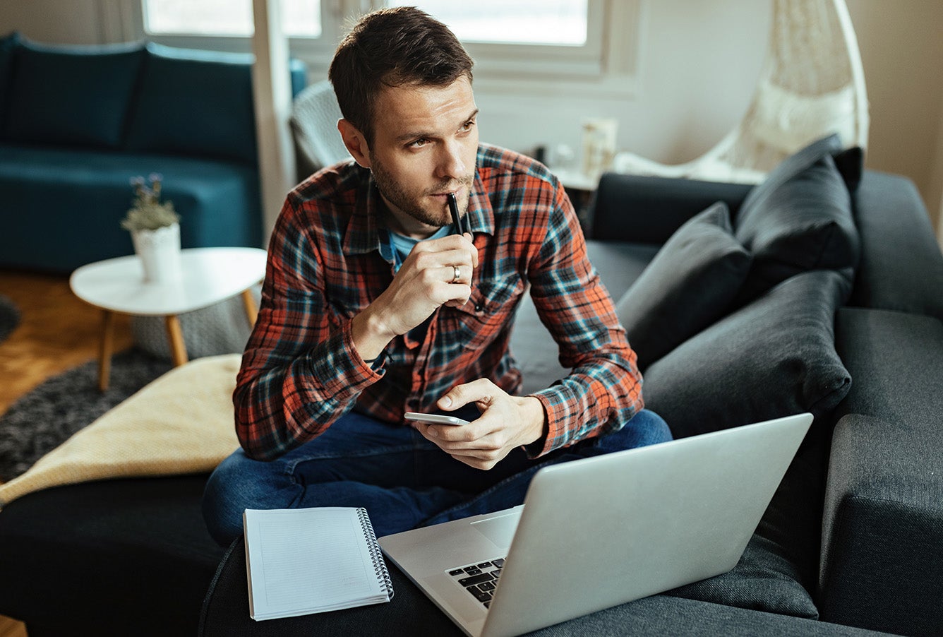 A young man holding a phone and working on a laptop