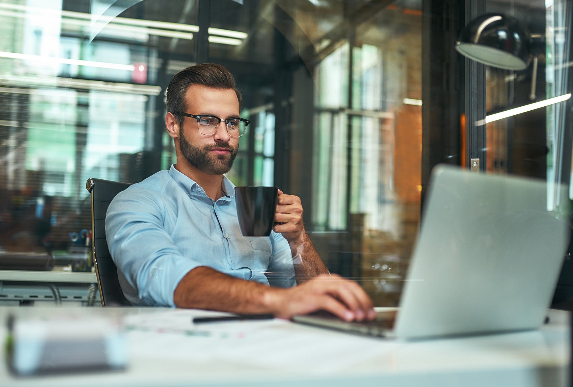 A man drinking coffee in front of his computer