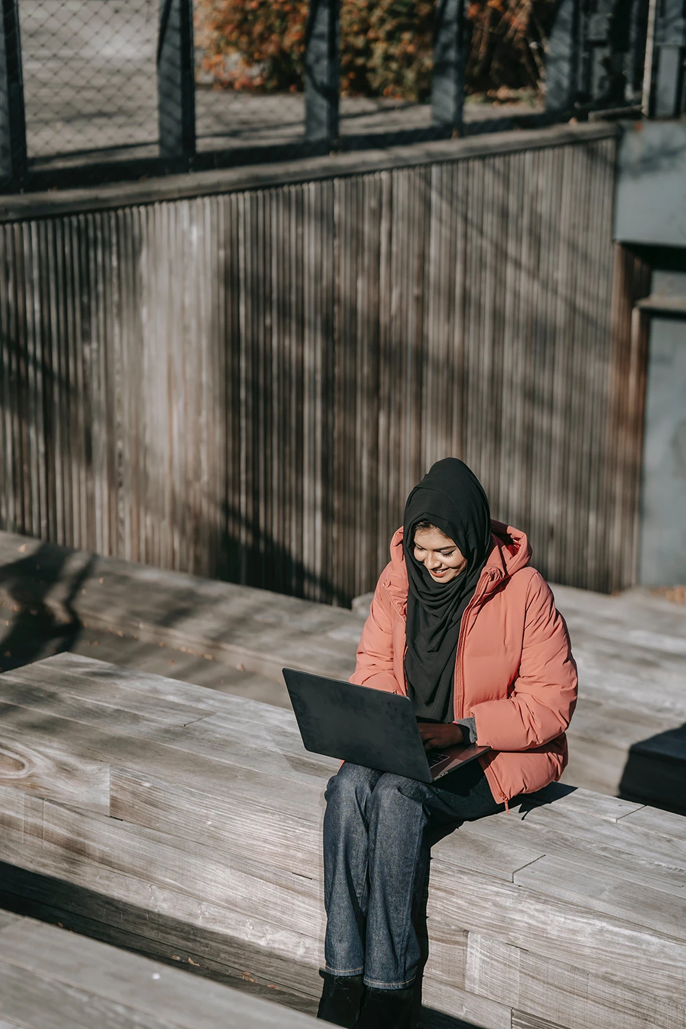 A young woman smiling at a laptop, sitting on stairs outside