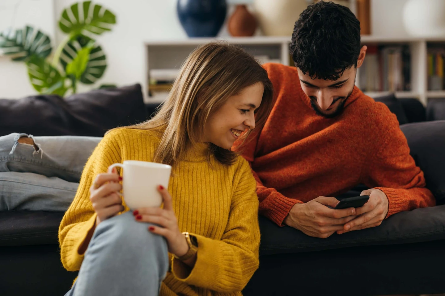 Man and woman with coffee cup on couch looking at phone