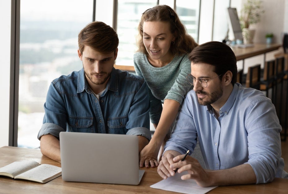 A group of three people looking at one laptop in an office