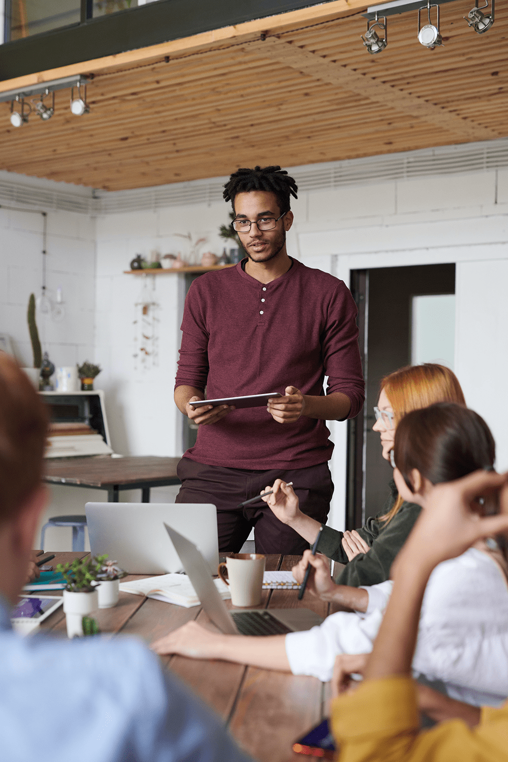 A black man with a tablet giving a speech in front of a group of people in an office
