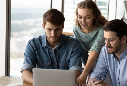 A group of people looking at one laptop in an office