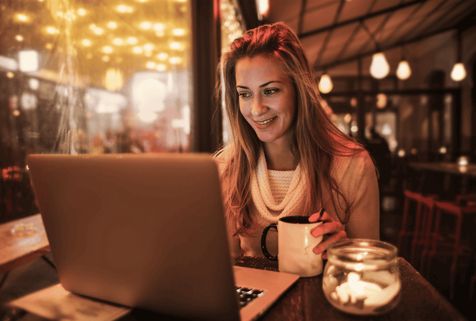 A young smiling woman working on her laptop in a coffee shop